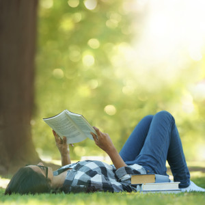 Shot of a young woman lying on grass and reading a book